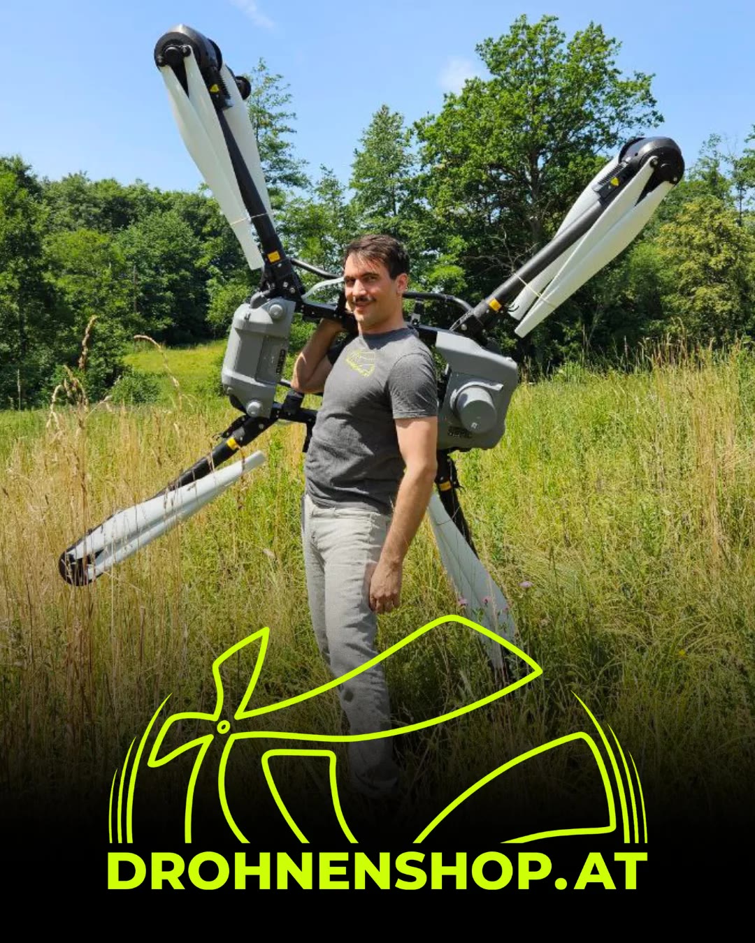 Michael Hackl mit einer großen Drohne auf den Schultern, hinter ihm Wiese und Waldrand.
